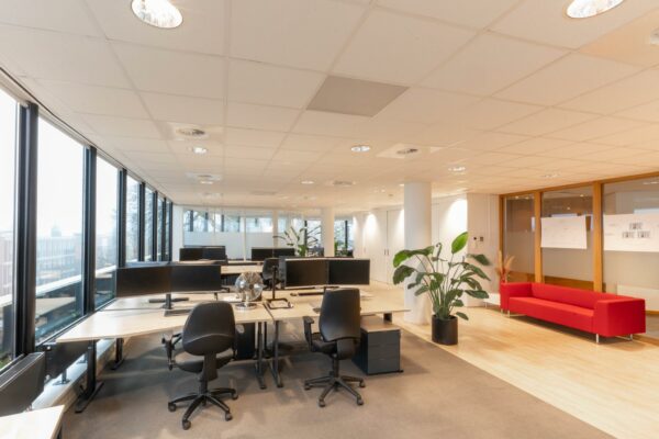 Modern en licht kantoorinterieur aan de 1e Hogeweg met bureaus, computers, planten en een rode bank in de wachtruimte.